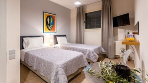 A hotel room with two beds, a television, a desk with a computer, and a window with curtains. - Kitries Summer Getaway - Eden Sandy Suite (West Mani)