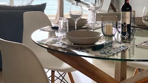 A dining area with a glass table, white chairs, and a bottle of wine. - Seafront Kalamata Haven - Blue Luxury Suite (Kalamata)