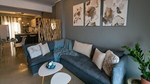 A modern living room with a grey sofa, a white coffee table, and abstract artwork on the wall. - Seafront Kalamata Haven - Blue Luxury Suite (Kalamata)