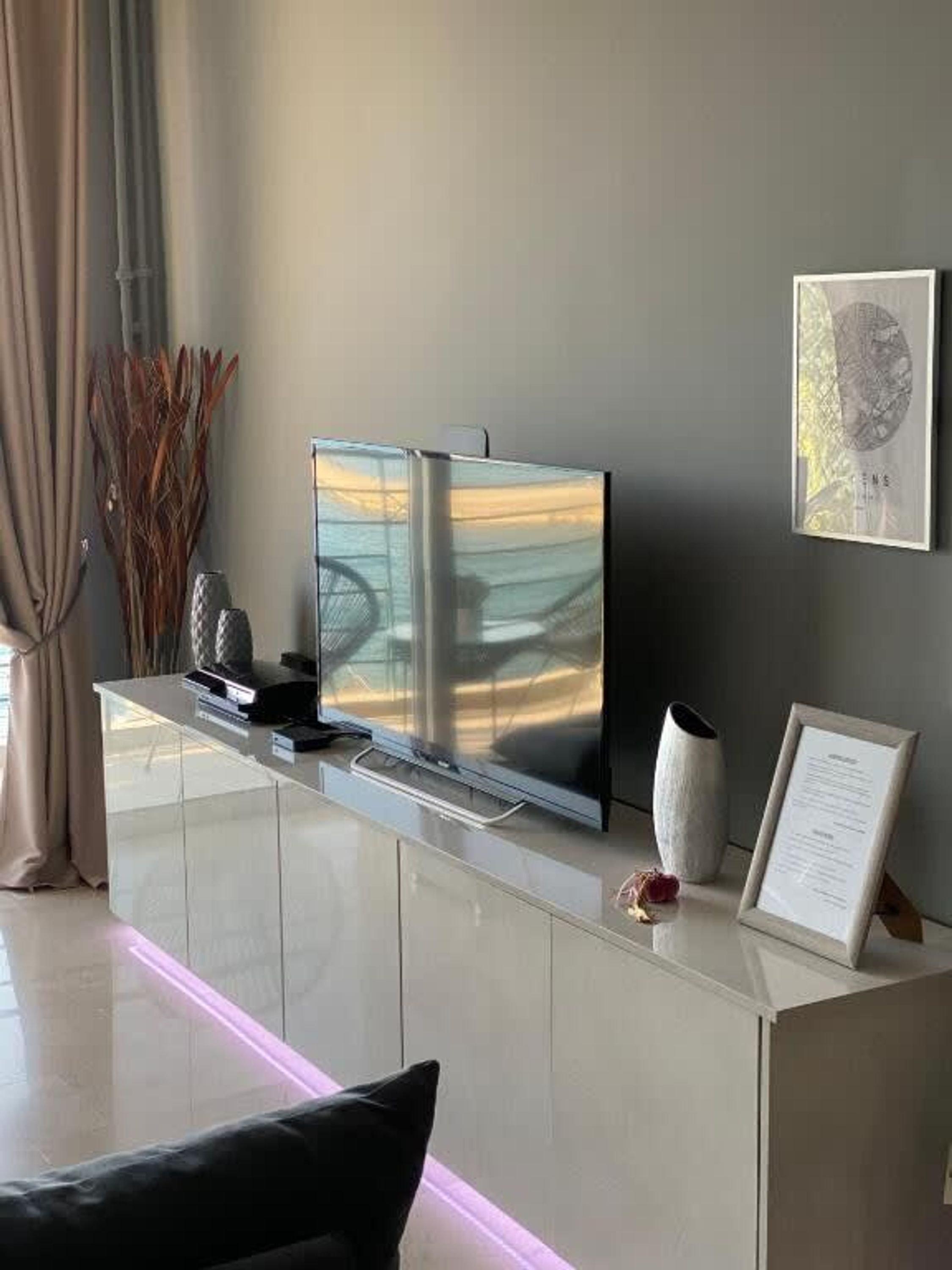 Un salon moderne doté d’un meuble de rangement épuré et blanc, comprenant un téléviseur à écran plat et une œuvre d’art encadrée accrochée au mur.