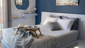 A modern bedroom with a bed, bedside tables, a hanging light fixture, and artwork on the wall. - Seafront Kalamata Haven - Blue Luxury Suite (Kalamata)