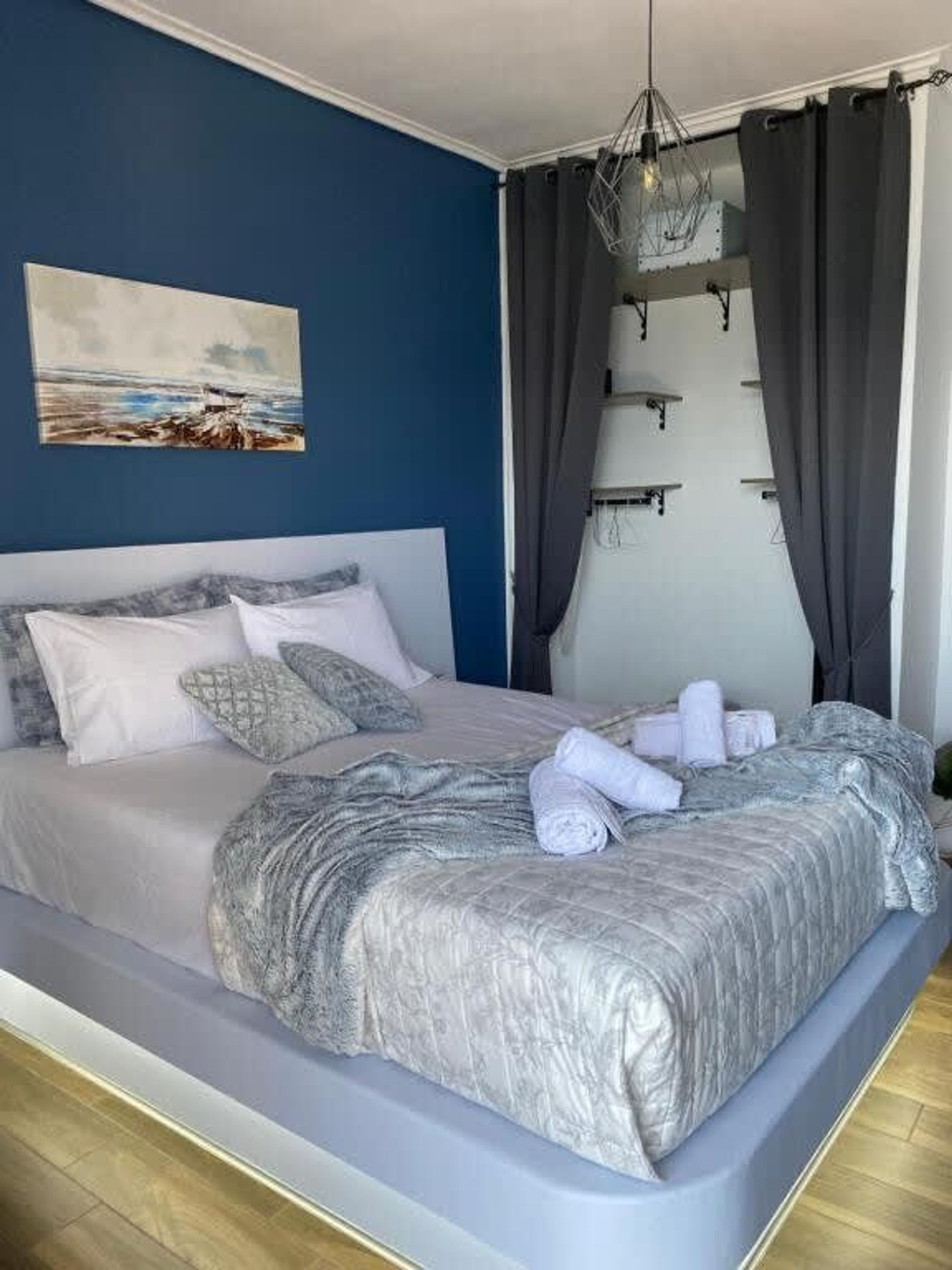 Ein ordentlich bezogenes Bett mit Kissen und Decke, ein Bild an der Wand und eine Pendelleuchte.