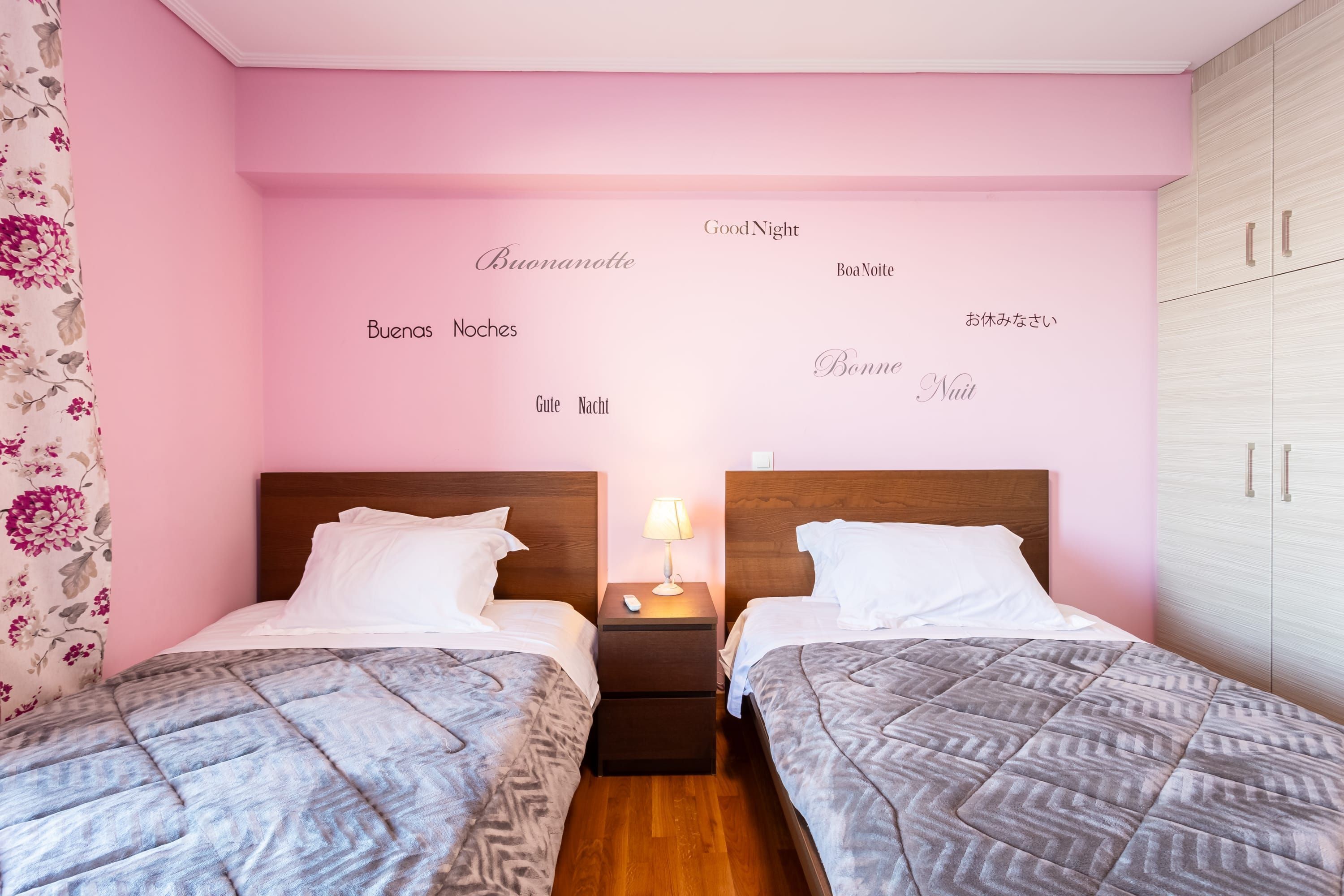 Une chambre avec deux lits, une table de chevet avec une lampe et un mur orné de messages « Bonne nuit » dans différentes langues.