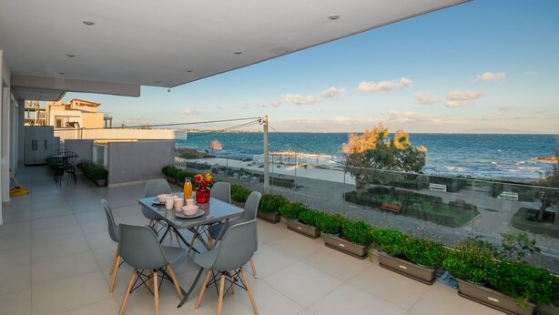 Ein moderner Balkon mit Meerblick, ein Essbereich mit Stühlen und einem Tisch sowie Kübelpflanzen.
