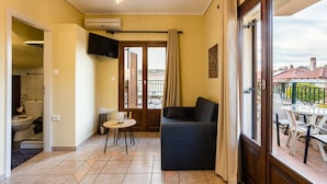 A living room with a sofa, a small round table, and a TV. There is a balcony with outdoor furniture. - Stoupa Oasis - Spitiko Garden Getaway (West Mani)