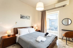 Une chambre d’hôtel avec un lit, des lampes de chevet, un miroir rond, une chaise et une fenêtre avec des rideaux.