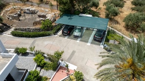 An aerial view of a parking area with three cars, a covered structure, and surrounding greenery.