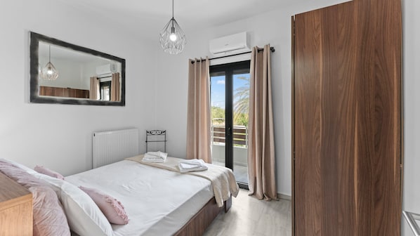 A bedroom with a bed, a wooden wardrobe, a radiator, a hanging light fixture, a window with curtains, and an air conditioning unit.