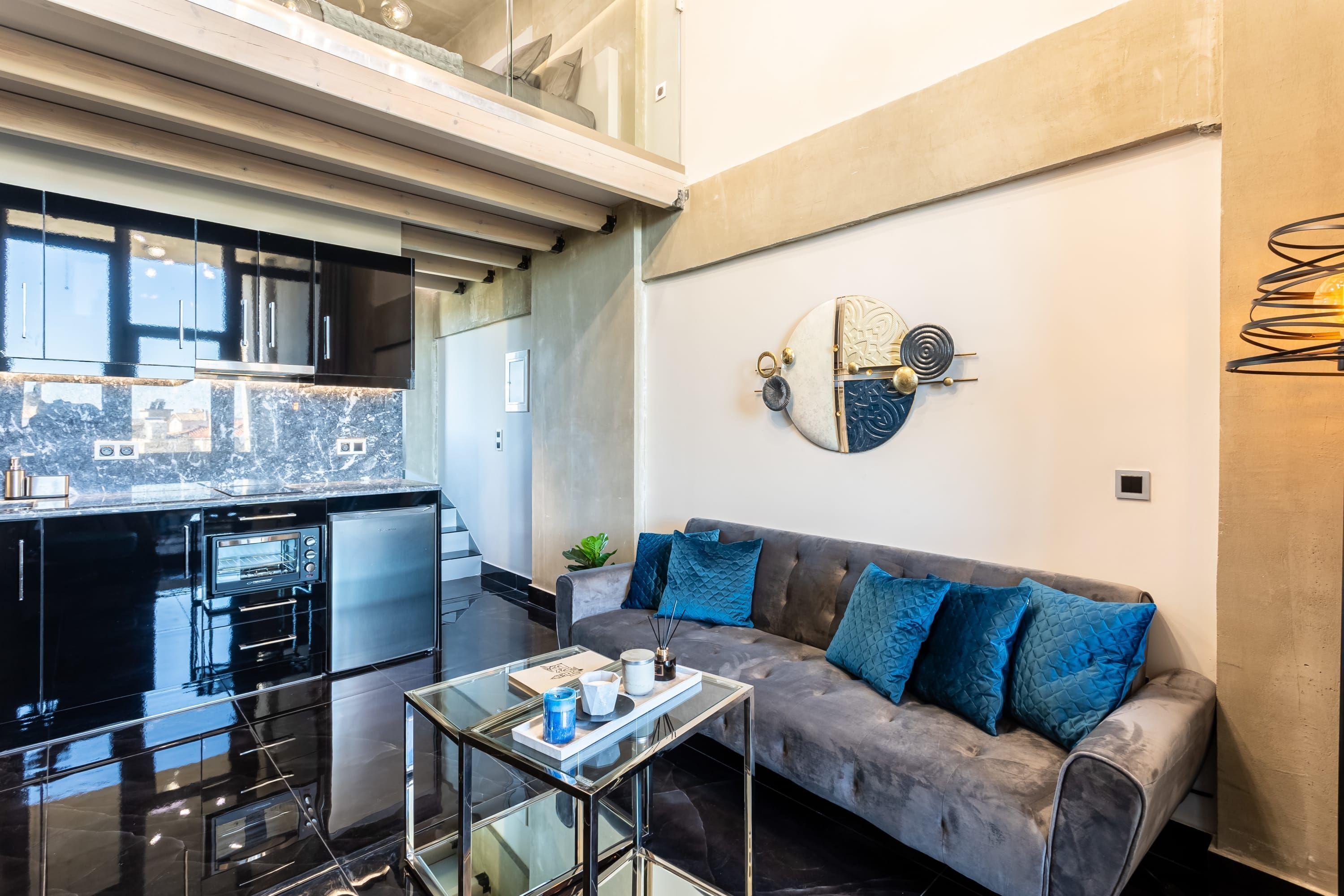 Una cucina moderna con mobili neri e forno integrato, un tavolino da caffè in vetro con un vassoio e un divano grigio con cuscini blu.