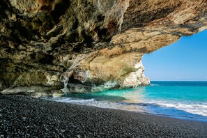 Une grotte rocheuse s’ouvrant sur une plage aux eaux turquoise et cristallines.