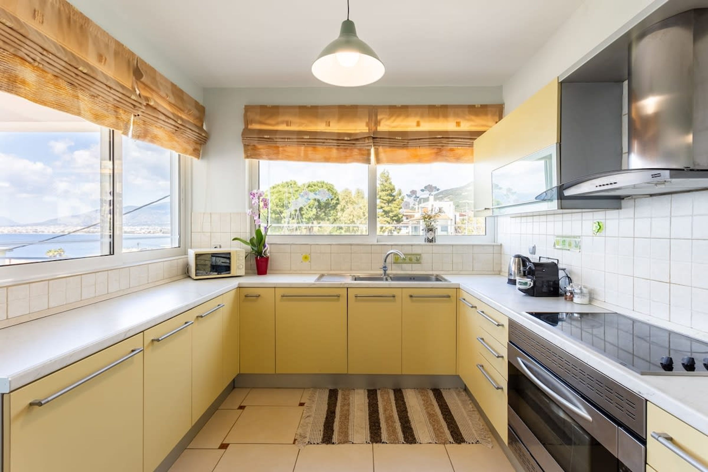 A modern kitchen with yellow cabinets, a stainless steel range hood, a microwave, and a large window with a view of the city.
