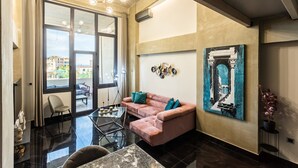 A modern living room with a pink sofa, a glass coffee table, and a large window offering a view of the outdoors. - Ventiri Lofts - Luxury Penthouse w Home Cinema (Kalamata)