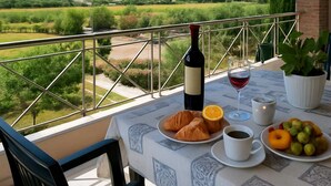 A balcony with a table set for breakfast, including croissants, fruit, and beverages, overlooking a scenic landscape.