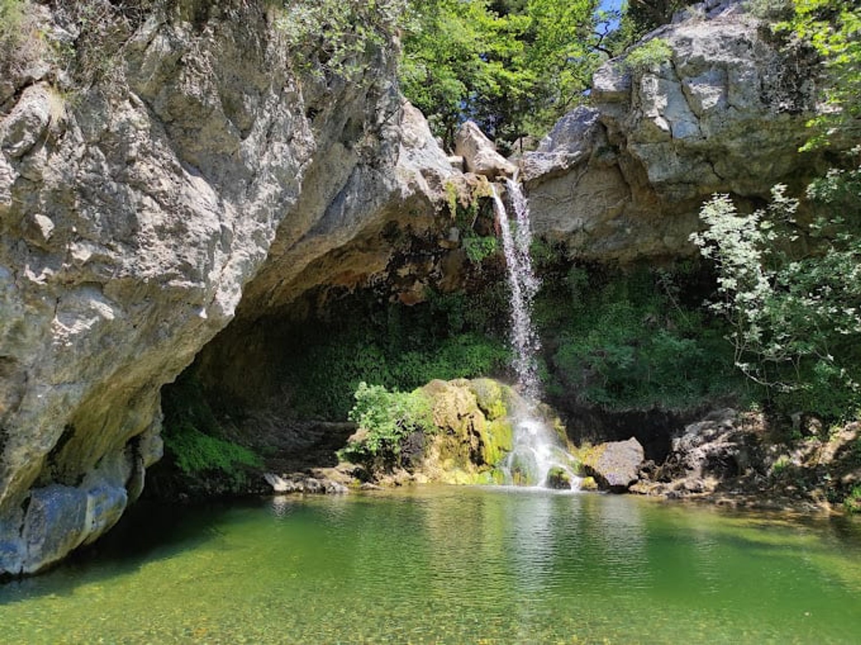A natural cave with a waterfall and a pool of water at its base.