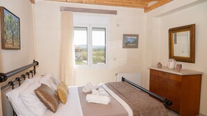 A bedroom with a bed, a dresser, a window with a view, and a painting on the wall.