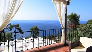 Un balcon avec vue sur la mer, des rideaux blancs et un canapé en osier.