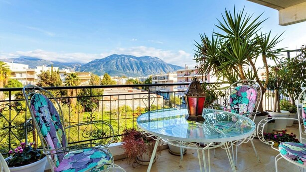A balcony with a glass table and chairs, a potted plant, and a view of mountains. - Bright Comfy Flat Near the Beach the City Center (Kalamata)
