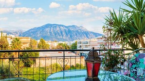 A balcony with a view of a mountain, a glass table, and a decorative lantern. - Bright Comfy Flat Near the Beach the City Center (Kalamata)