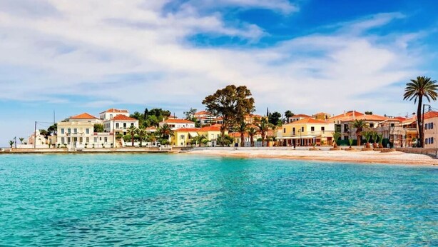 A coastal town with buildings along the waterfront, clear blue water, and a palm tree. - Vibrant Spetses - Mata Colorful Nest (Spetses)