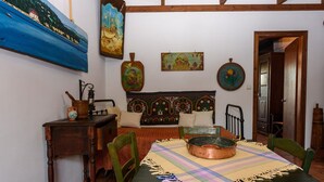 A dining area with a wooden table, chairs, and a colorful tablecloth. There are paintings on the walls and a rustic wooden bench. - Eros Cozy Perfect Location Panoramic sea View (Pylos-Nestoras)