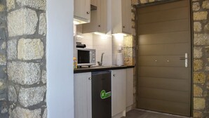 A compact kitchen with white cabinets, a microwave, a dishwasher, and a stone wall.