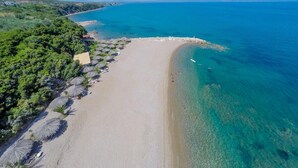 Vista aérea de una playa con aguas turquesas cristalinas, una orilla de arena y una hilera de sombrillas.