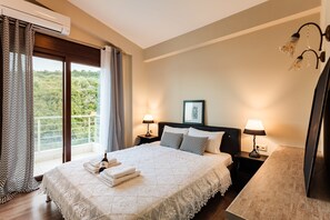 Un dormitorio con una cama grande, dos mesitas de noche con lámparas, una ventana con cortinas y vistas a zonas verdes.