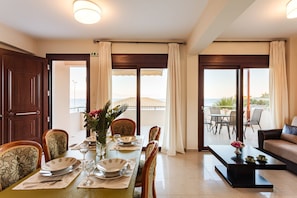 Un comedor con una mesa dispuesta para cuatro, sillas, una mesita de centro y vistas al mar a través de amplias ventanas.