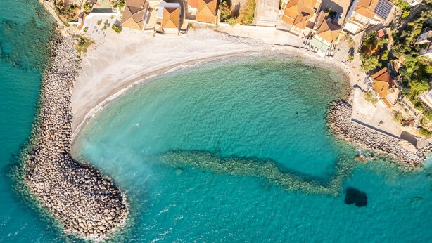 An aerial view of a coastal area with a beach, clear turquoise waters, and a rocky shoreline. - Seaside Family Haven - Avia s Spacious Getaway (West Mani)