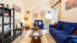 A living room with a blue sofa, a coffee table with a vase, a bookshelf, and a blue armchair. - Seaside Family Haven - Avia s Spacious Getaway (West Mani)
