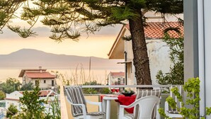 A balcony with white chairs and a table, overlooking a body of water and buildings. - Seaside Family Haven - Avia s Spacious Getaway (West Mani)