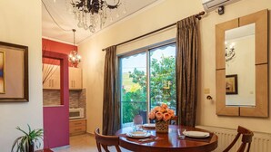A dining area with a round table, chairs, a vase of flowers, and a view of greenery outside. - Stylish Seaside Home - Fully Equipped big Terrace (Kalamata)