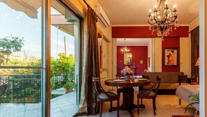 A room with a dining table, chairs, a chandelier, a sofa, and a balcony with a view of greenery. - Stylish Seaside Home - Fully Equipped big Terrace (Kalamata)