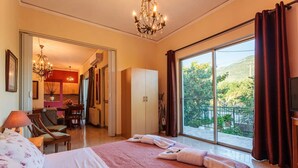 A hotel room with a large bed, a chandelier, a balcony with a view, and a dining area visible through an open door. - Stylish Seaside Home - Fully Equipped big Terrace (Kalamata)