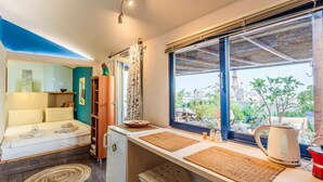 Une chambre de taille modeste comprenant un lit, un coin cuisine et une grande fenêtre donnant sur un paysage verdoyant.