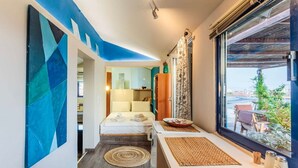 Une chambre d’hôtel étroite, avec un lit, une petite table, une fenêtre donnant sur un paysage agréable et un mur décoré de motifs géométriques bleus.