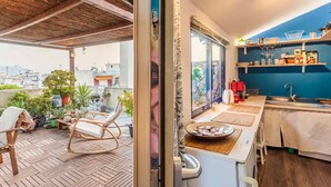 Une cuisine compacte avec vue sur la ville, un coin repas avec une table et des chaises, et un petit balcon agrémenté d’une chaise et de plantes.