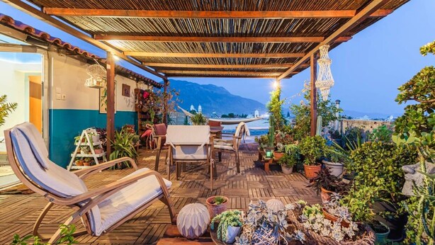 Un espace extérieur abrité, aménagé avec du mobilier en bois, des plantes en pot et offrant une vue sur la mer.