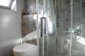 A bathroom with a toilet, a shower with a glass door, and patterned tiles on the walls. - Coastal Stone Residence With Spectacular Scenery (West Mani)