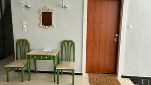 Una habitación con puerta de madera, una mesita con dos sillas, un espejo y apliques en la pared.
