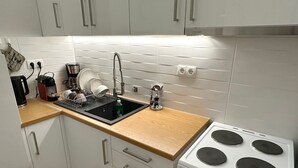 Una cocina moderna con armarios blancos, un lavamanos negro, una campana de acero inoxidable y una estufa blanca.