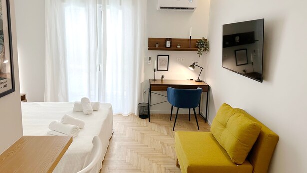 Una habitación de hotel moderna con una cama, un escritorio, una silla, un sofá y un televisor.