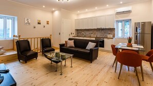 A modern living room with a black sofa, two armchairs, a glass coffee table, and a dining area with a table and orange chairs. - Valira Cozy Maisonette - Relaxing Vibes Getaway (Messini)