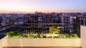 Varanda com plantas e vista para o horizonte urbano ao pôr do sol.