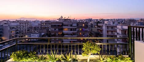 A balcony with plants and a view of a cityscape at sunset.
