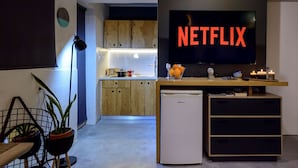 Uma cozinha moderna com armários de madeira, máquina de lavar louça embutida e uma grande TV de tela plana exibindo o logotipo da Netflix.