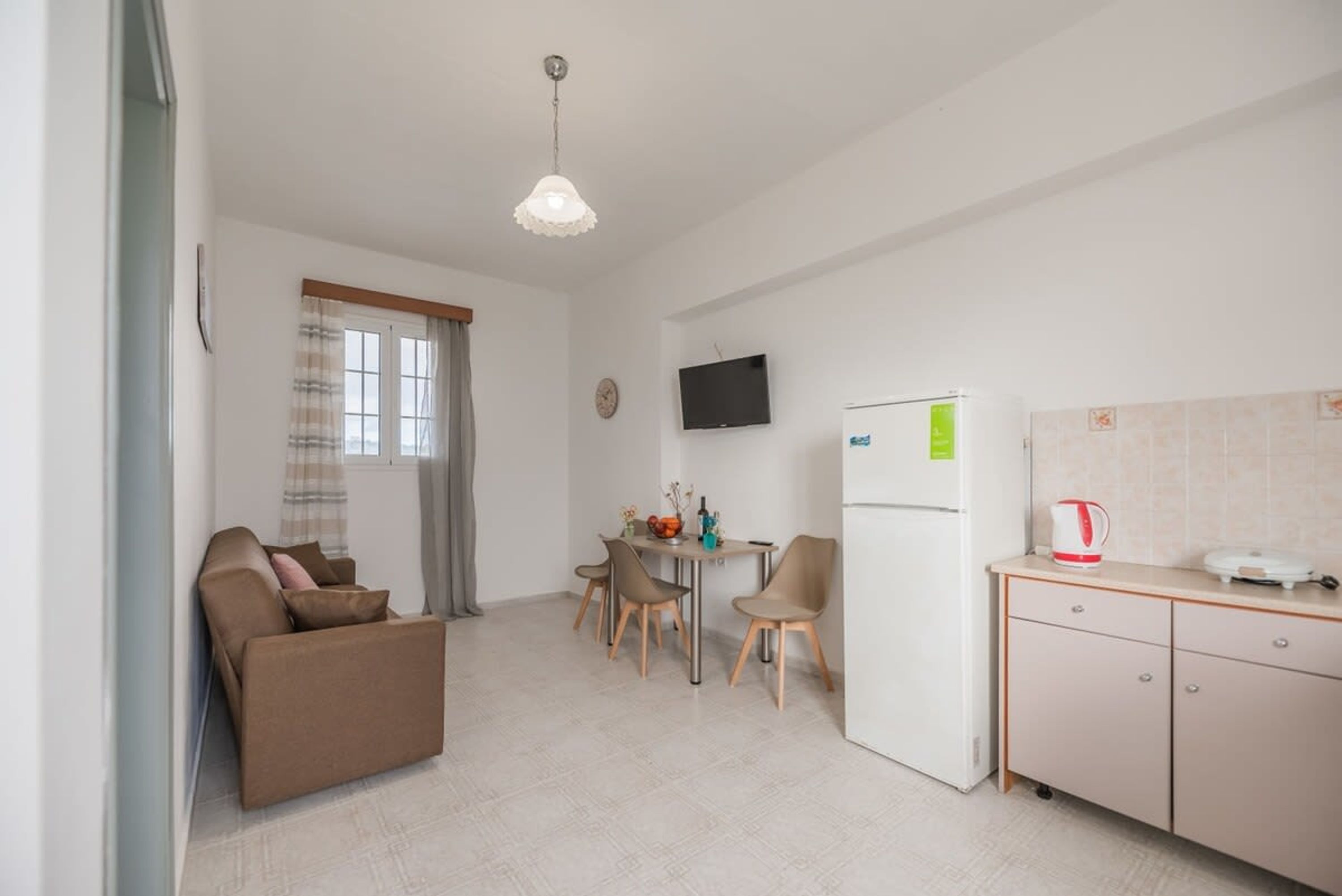 Espai habitable reduït amb sofà, taula de dinar, cadires, televisió, nevera i zona de cuina.