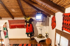 Una habitación con techo de madera, televisor, textiles tradicionales y un maniquí vestido con traje típico.