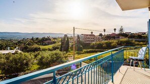 Un balcon doté d’une balustrade bleue, d’où l’on peut admirer un paysage composé d’arbres, de bâtiments et de montagnes.