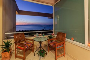 A balcony with two wooden chairs and a small table, overlooking a scenic view of a body of water and distant mountains during twilight.
